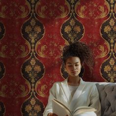 a woman reading a book while sitting on a couch in front of a red wall