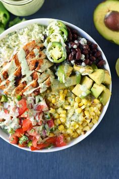 a white bowl filled with mexican food next to avocado