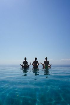 three people are sitting in the water with their backs to each other and holding hands