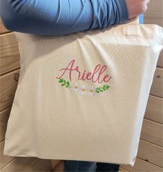 a person holding a personalized tote bag with daisies and leaves on it