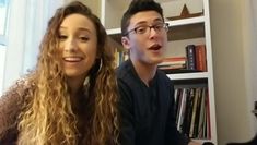 a man and woman sitting next to each other in front of a book shelf filled with books