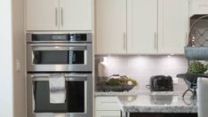 a kitchen with white cabinets and stainless steel appliances, including a double oven in the center