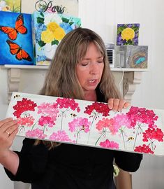 a woman holding up a piece of paper with flowers painted on it