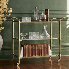 a shelf with books and glasses on it in front of a vase filled with flowers