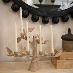 some candles are sitting on a table next to a mirror and vase with leaves painted on it