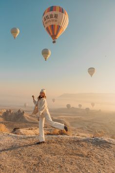 a woman standing on top of a hill next to hot air balloons in the sky