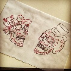 two skulls with hats on their heads sitting next to each other in front of a piece of paper