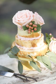 a three tiered cake sitting on top of a table with flowers and greenery