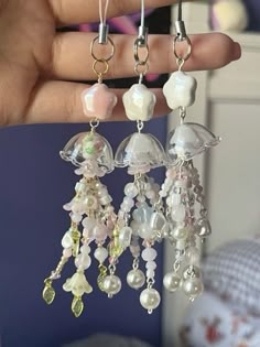 a person is holding three dangling earrings with pearls and swarongs on them