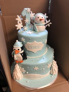 a blue and white cake with snowmen on top in a box for someone's first birthday