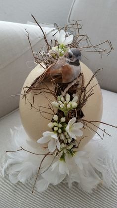 a bird sitting on top of an egg decorated with branches and flowers in the center