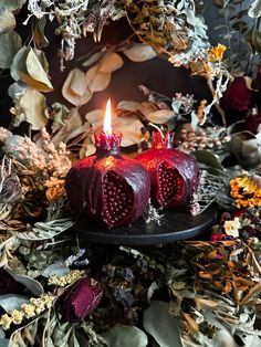 two red candles sitting on top of a black plate surrounded by flowers and foliages