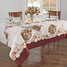 a dining room table with a thanksgiving themed table cloth and place settings on the table