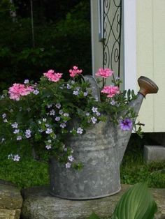 a watering can filled with pink flowers sitting on top of a rock wall next to a door