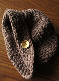 a crocheted hat with a gold button on it sitting on a wooden table