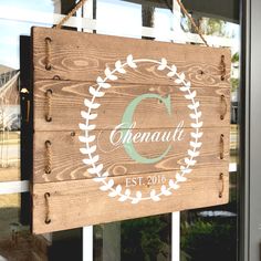 a wooden sign hanging from the side of a window next to a door with a wreath on it