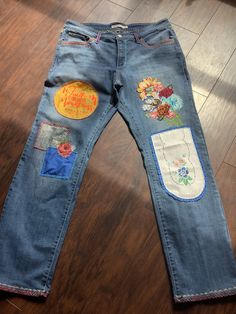 a pair of blue jeans with patches and flowers on the side, sitting on a wooden floor