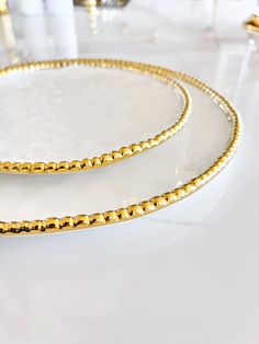 two white plates with gold trim on them sitting on a counter top next to each other