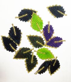 six beaded leaves are arranged on a white surface, one is green and the other is purple