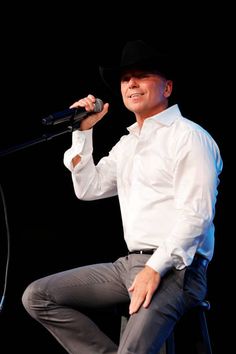 a man in a white shirt and black hat is sitting on a stool while holding a microphone