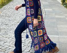 a woman standing on the sidewalk with her legs crossed and wearing a crocheted shawl