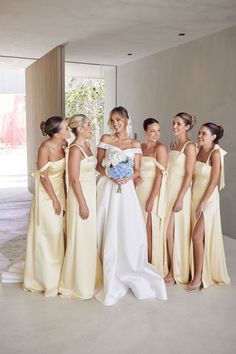 a group of women standing next to each other in front of a wall wearing dresses