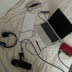 an open laptop computer sitting on top of a bed next to headphones and batteries