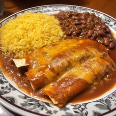 a plate with beans, rice and enchilada on it sitting on a table