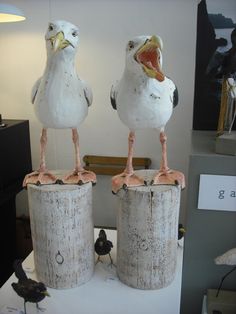 two white birds sitting on top of wooden stumps in front of a wall mounted clock