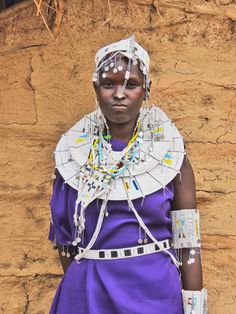 a woman in a purple dress and headdress standing next to a stone wall