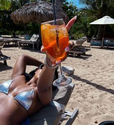 a woman laying on the beach with a drink in her hand