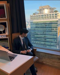 a man sitting at a desk in front of a window with a laptop on it