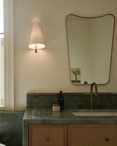 a bathroom sink with a large mirror above it and a light on the wall behind it