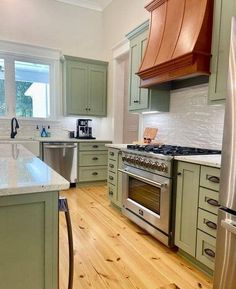 a kitchen with green cabinets and stainless steel appliances, wood flooring and white counter tops