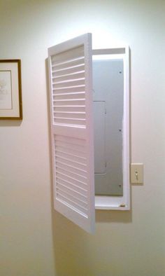 an open window in the wall with shutters on it and a framed picture above