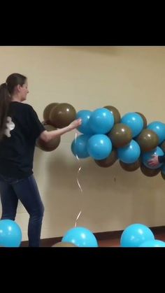 two people standing in front of blue and brown balloons with one person reaching for the balloon