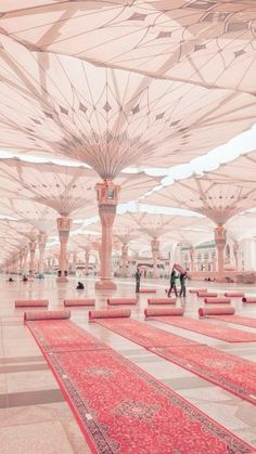 people are walking through an open area with many umbrellas over the floor and rugs on the ground