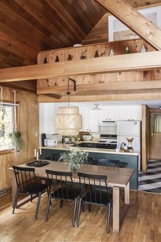 a dining room table and chairs in a kitchen with wooden walls, flooring and beams on the ceiling