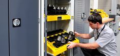 a man is working on an electrical device in a storage cabinet with yellow bins