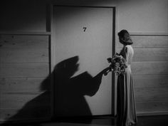 a woman standing in front of an open door with her shadow on the wall behind her