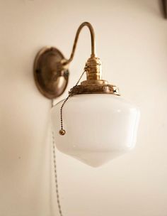 an old fashioned wall light hanging from the side of a white wall with a chain attached to it