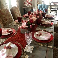 a dining room table set with red and white plates, silverware and napkins