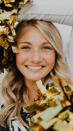 a smiling young woman wearing a cheerleader's uniform and gold pom - poms