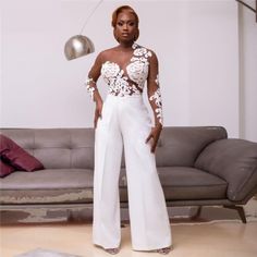 a woman standing in front of a couch wearing white pants and a top with flowers on it