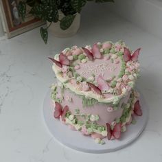 a heart shaped cake with pink flowers and butterflies on it sitting on a white table