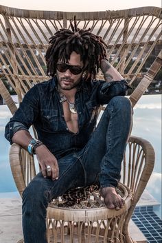 a man with dreadlocks sitting in a wicker chair next to a pool