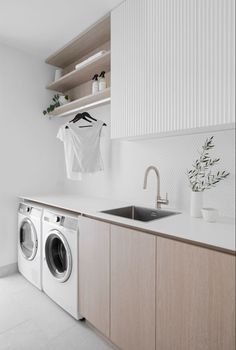 a washer and dryer in a white laundry room with wooden cabinets, hanging clothes on the wall