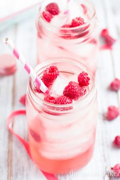 two mason jars filled with raspberries on top of a white wooden table next to pink ribbon