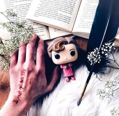 a person with their hand on an open book next to a fake doll and feather