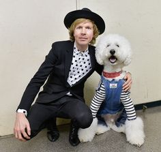 a man in a suit and tie holding a white dog wearing a hat with stripes on it